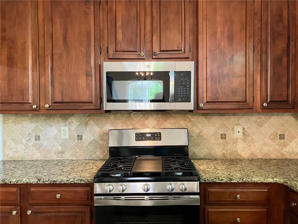 Kitchen with tasteful backsplash, appliances with stainless steel finishes, and light stone counters