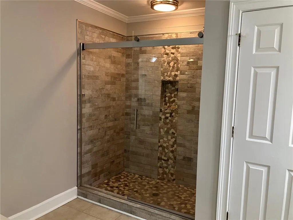 Bathroom with crown molding, a shower with shower door, and tile flooring