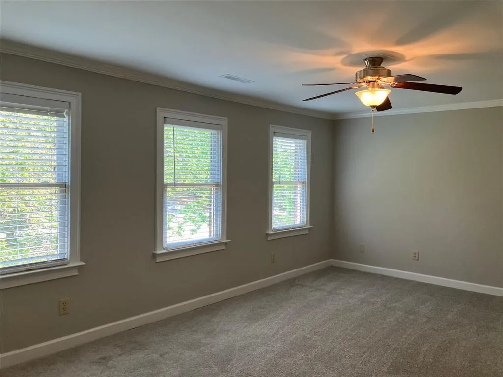 Carpeted spare room featuring plenty of natural light, ceiling fan, and ornamental molding