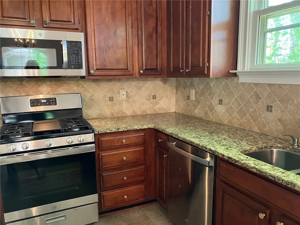 Kitchen with appliances with stainless steel finishes, backsplash, light tile floors, and light stone counters