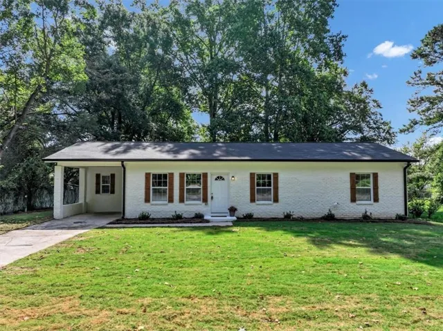 White painted brick exterior with brown shutters, a carport, a dark shingle roof, and a concrete driveway