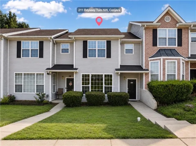 Gray two-story townhome featuring a front lawn and a concrete walkway