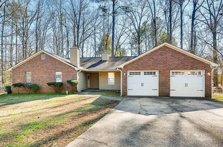 Brick facade residence with a two-car garage, featuring white paneled garage doors with decorative hardware, and a paved driveway