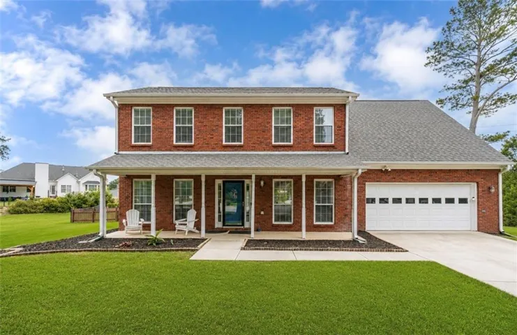 Traditional brick-front residence featuring a covered front porch, white window frames, an attached two-car garage, and a concrete driveway