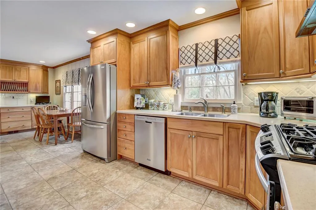 Kitchen with custom range hood, light tile floors, ornamental molding, stainless steel appliances, and sink