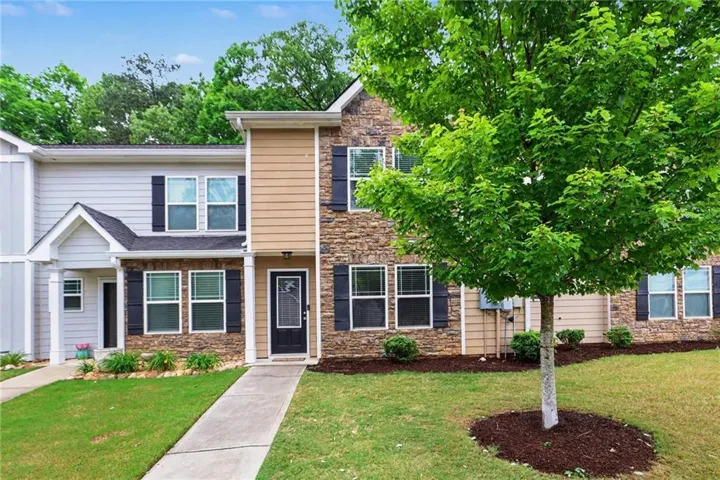 Stone and siding exterior with dark shutters, front entry with transom window, covered porch, concrete walkway, and established landscaping