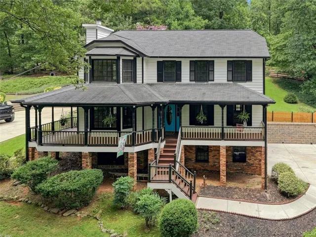 Two-story residence featuring a covered front porch, brick foundation, bay window, white siding, and a vibrant blue entry door