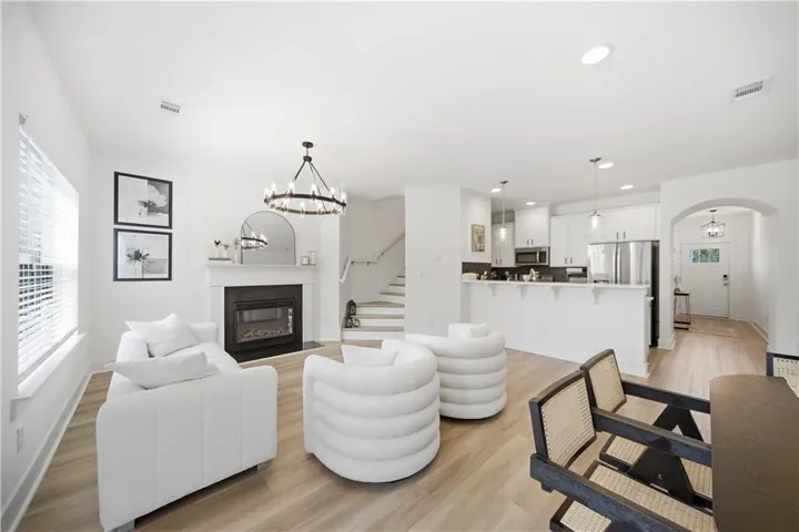 Spacious open-concept living area featuring wood-finish flooring, a contemporary fireplace with a mantel, and a stylish chandelier