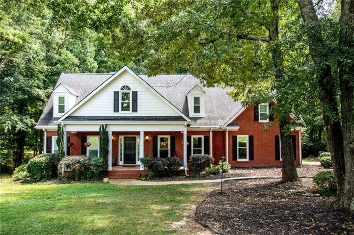 Charming Colonial-style residence featuring a brick exterior with white trim accents, a gabled roofline with dormer windows, and a covered front porch