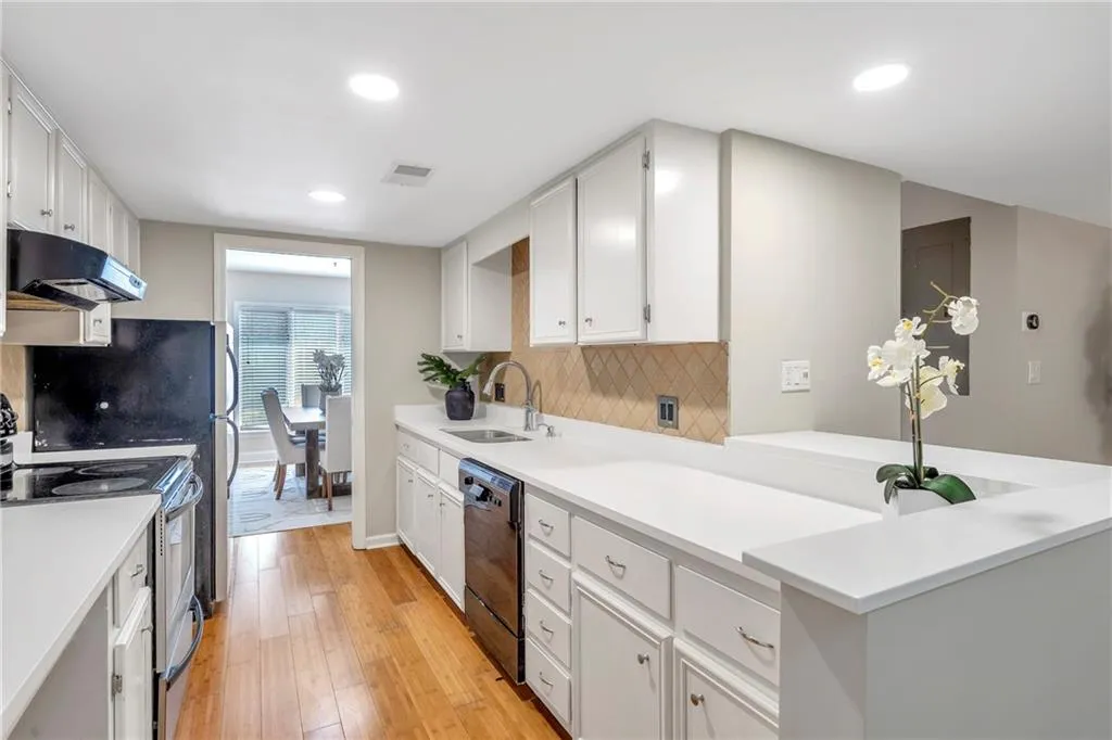 Kitchen with stainless steel range with electric cooktop, black dishwasher, ventilation hood, light wood-style flooring, and white cabinetry