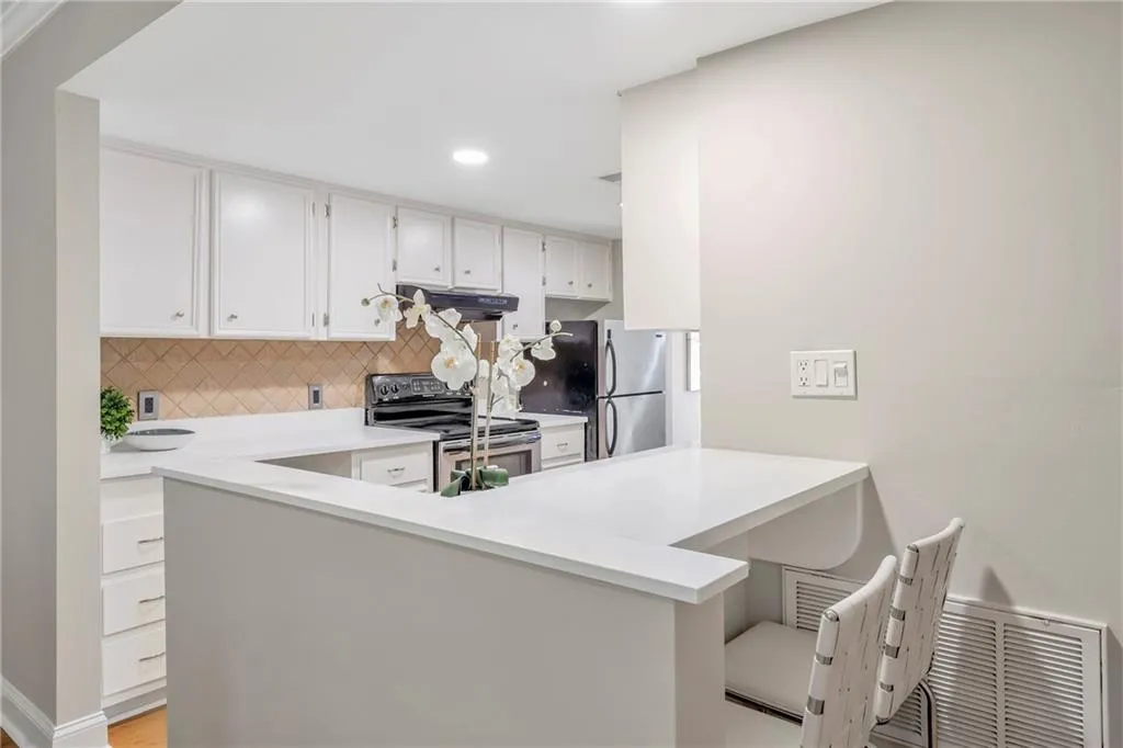 Kitchen with appliances with stainless steel finishes, under cabinet range hood, a peninsula, tasteful backsplash, and light countertops