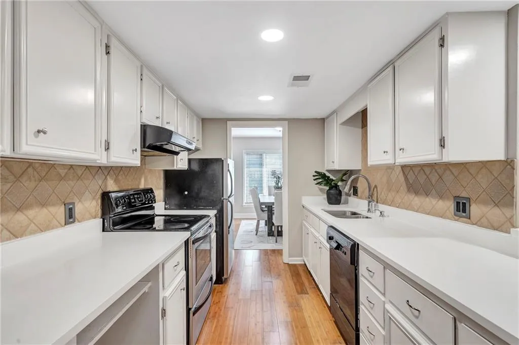 Kitchen featuring range with electric stovetop, dishwasher, under cabinet range hood, light wood-type flooring, and white cabinetry
