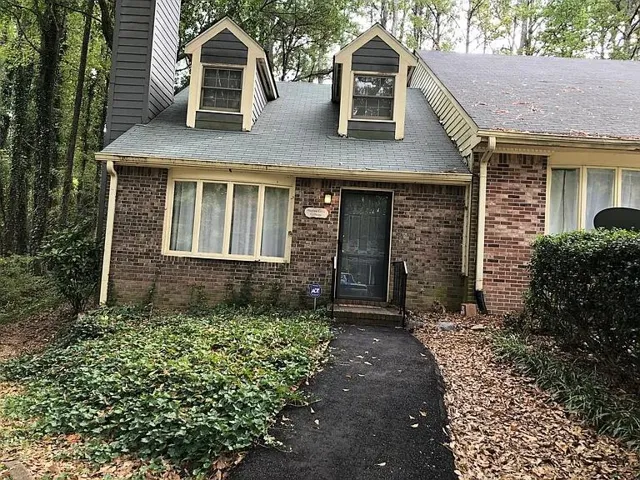 Brick facade residence featuring two dormer windows, a prominent chimney, and a dark asphalt pathway