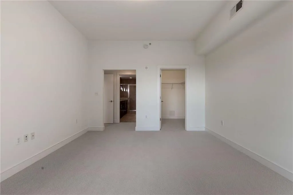 Unfurnished bedroom featuring a closet, a walk in closet, visible vents, light carpet, and baseboards