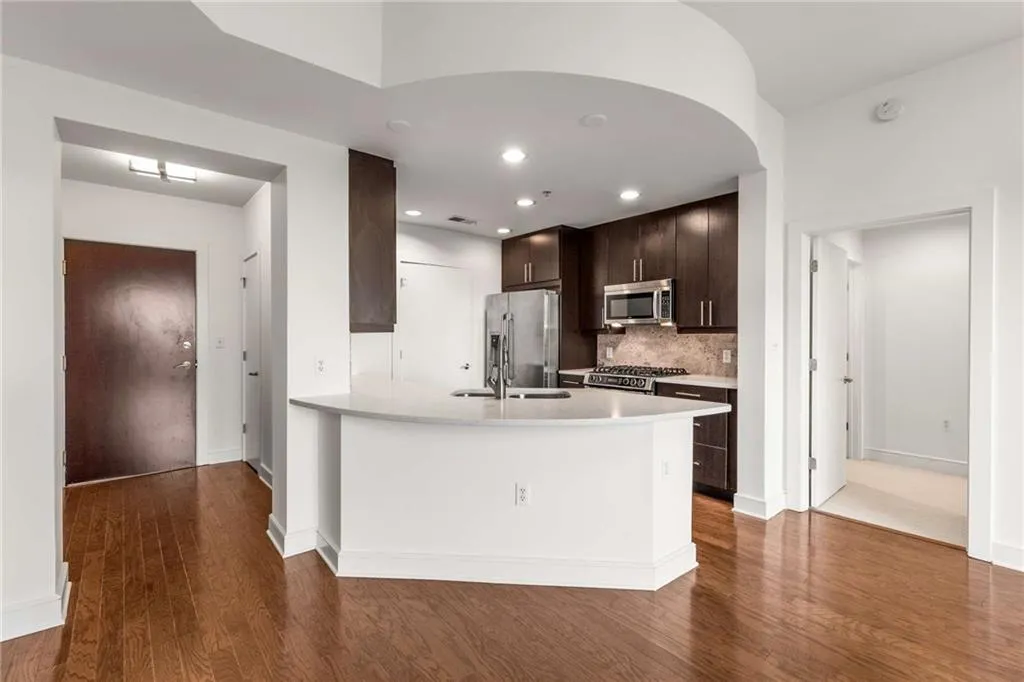 Kitchen featuring dark brown cabinetry, decorative backsplash, appliances with stainless steel finishes, light countertops, and dark wood-style flooring
