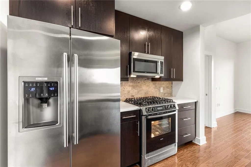 Kitchen with tasteful backsplash, baseboards, light wood-style flooring, light countertops, and appliances with stainless steel finishes