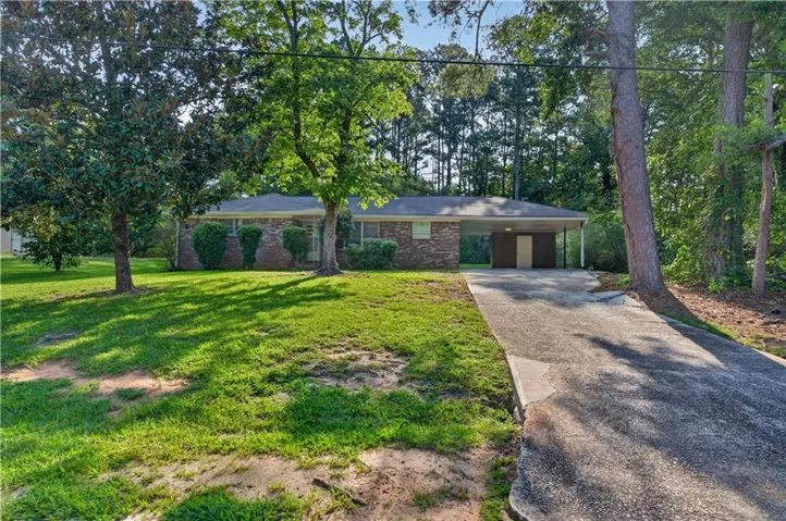 Brick exterior residence with a single-car carport, concrete driveway, and mature landscaping