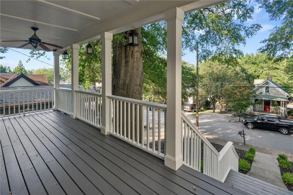 Covered porch with dark gray deck flooring, white railing, and ceiling fan