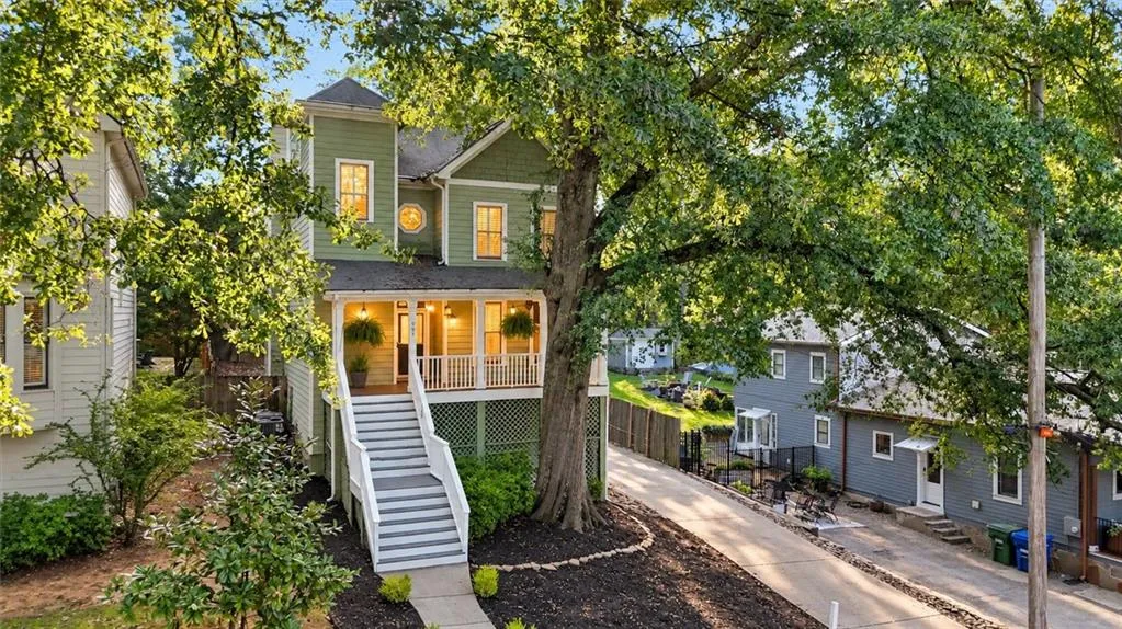 Two-story exterior with a covered front porch featuring white railings, a wide staircase, and a prominent mature tree
