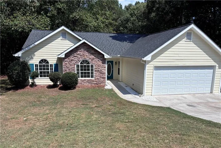 Yellow siding exterior with stone accent, a two-car garage, and arched windows