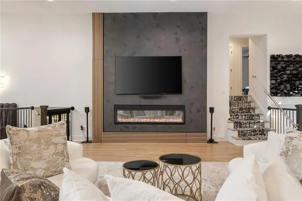 Feature wall with textured finish, integrated linear fireplace, light wood-finish flooring, and open staircase with patterned runner