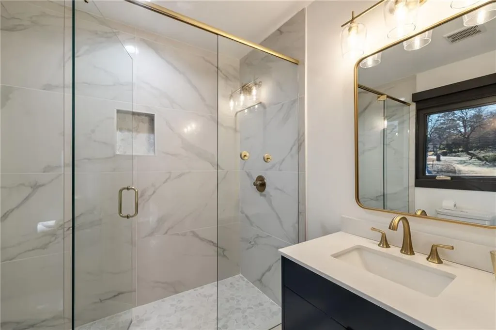 Glass-enclosed shower with a recessed niche, marble-look tile, and a mosaic tile floor