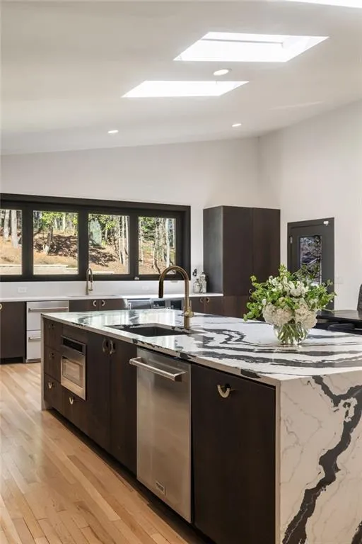 Kitchen featuring a waterfall-edge island with a black and white patterned countertop, integrated sink with a bronze-finish faucet, and stainless steel dishwasher