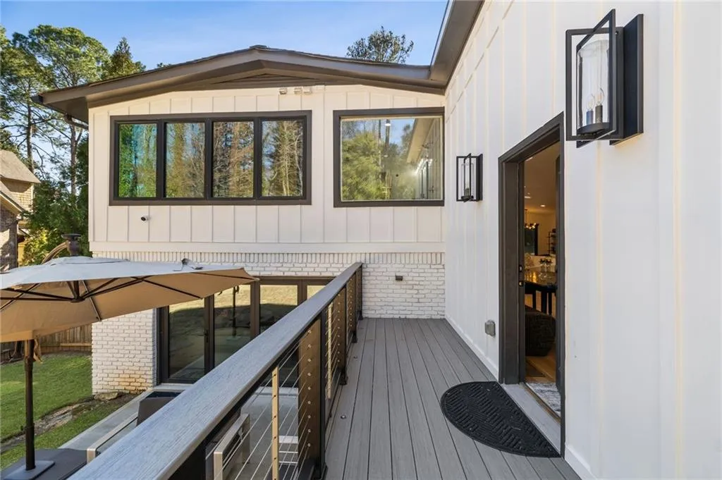 Exterior deck featuring a cable railing system, modern sconce lighting, and a white board-and-batten facade with brick accents
