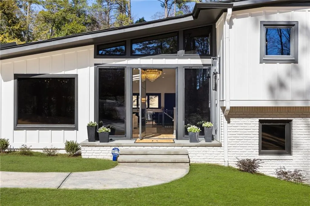 White board-and-batten siding with a dark trim, full-light glass double entry doors, transom windows, and white painted brick