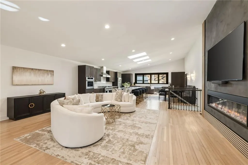 Vaulted ceilings with recessed lighting, skylights, wood-finish flooring, and a linear fireplace with a dark surround