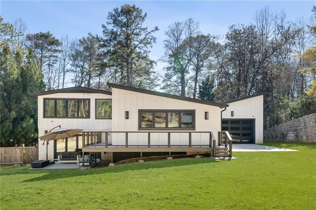 Contemporary white exterior with dark trim, expansive rear deck, ground-level patio, and attached garage