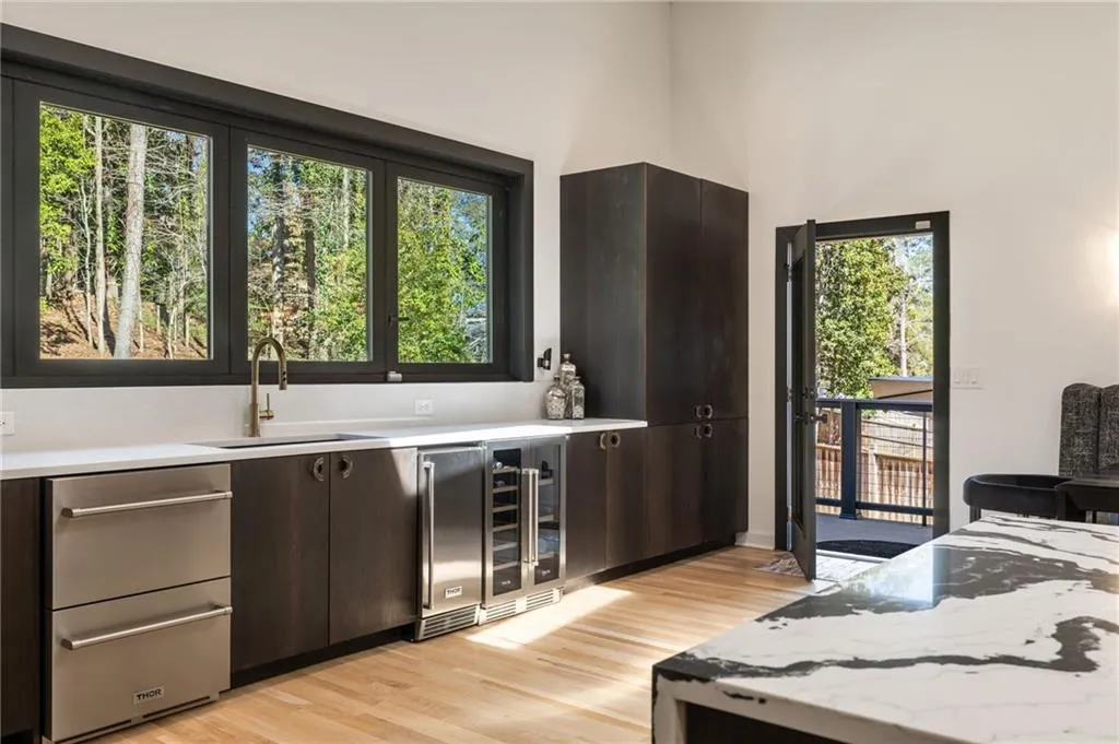 Integrated stainless steel appliances, dark wood-finish cabinetry, light wood-finish flooring, and a stone countertop with a contrasting pattern