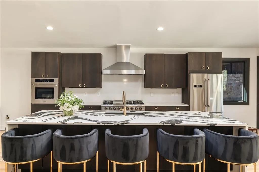 Kitchen island with a waterfall edge countertop, stainless steel appliances, dark wood-finish cabinetry, built-in oven, and a gas range