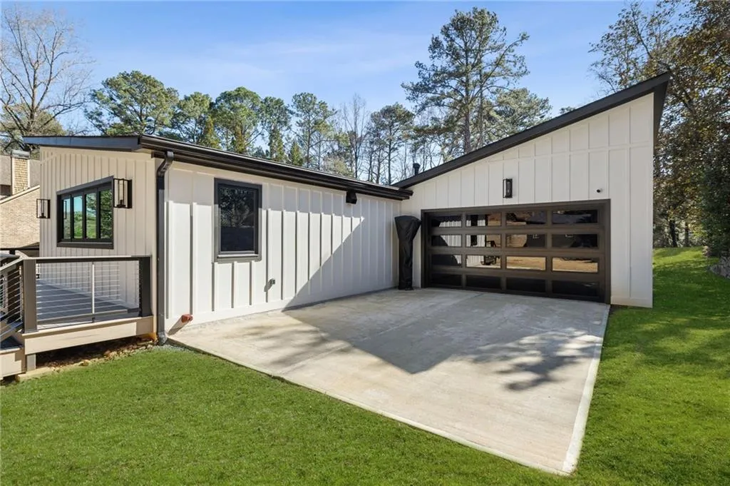 White vertical siding with black-framed windows, a glass-paneled garage door, an angled roofline, and a deck with metal railings