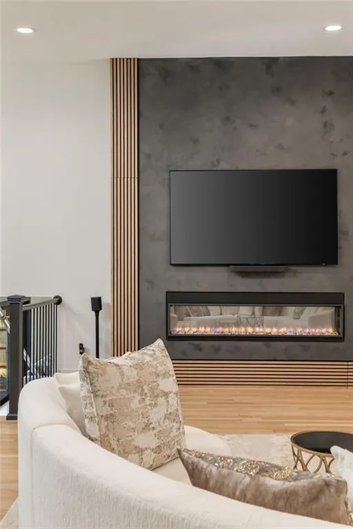 Recessed ceiling lighting, textured wall paneling, linear electric fireplace, wood-finish flooring, and black metal stair railings