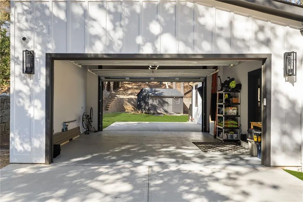 Board and batten exterior with modern sconces, concrete garage flooring, and a detached shed structure
