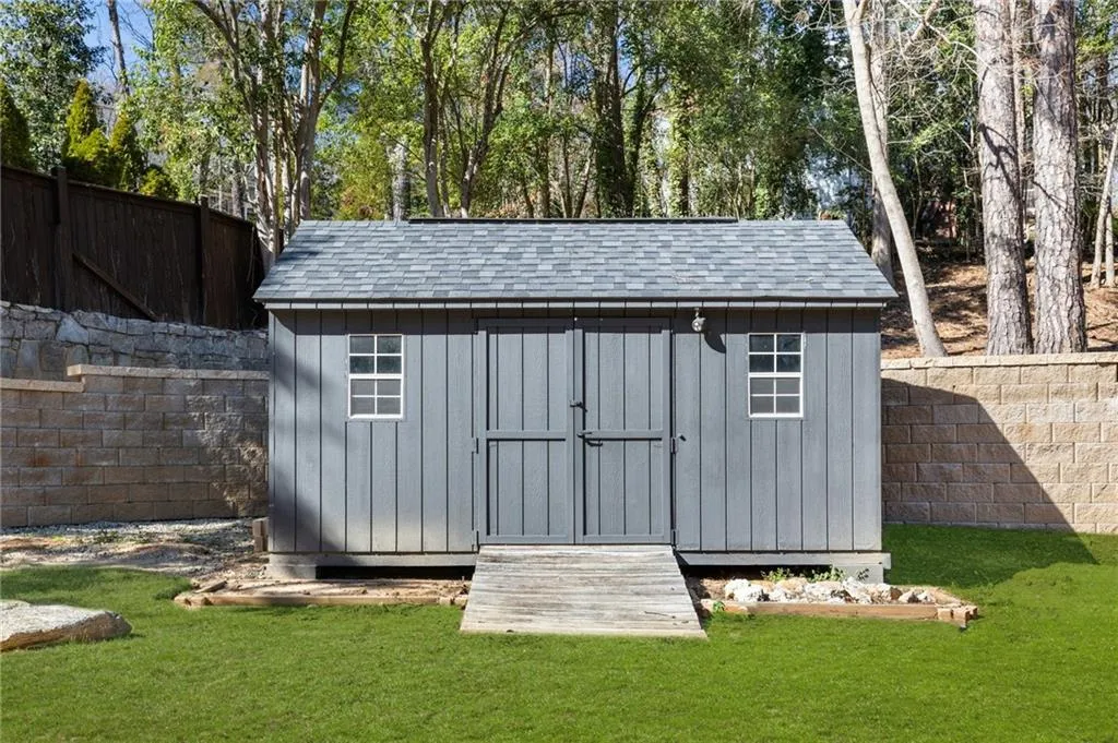 Detached shed with gray siding, a gray shingled roof, double doors, and two windows