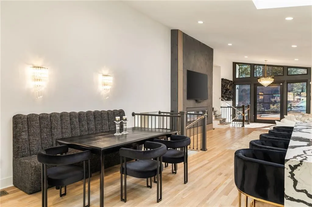 Hardwood flooring, integrated fireplace, wall-mounted light fixtures, full-height windows, and a large chandelier