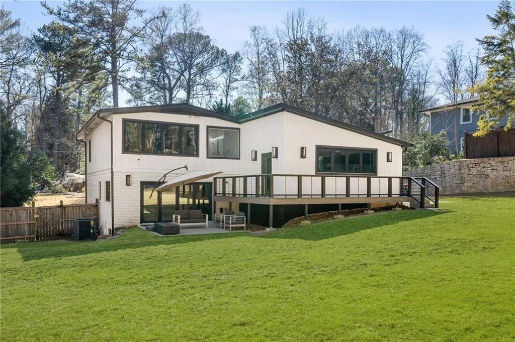Expansive green lawn, a white exterior with dark-framed windows, and a multi-level deck with glass panel railings