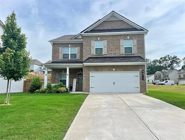 Two-story brick facade residence featuring a covered front porch with white columns, a two-car garage, and a concrete driveway