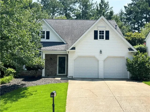 White siding exterior with a dark shingle roof, stone accent columns, and a two-car garage