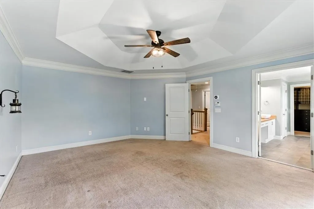 Unfurnished bedroom featuring crown molding, light carpet, connected bathroom, a tray ceiling, and ceiling fan