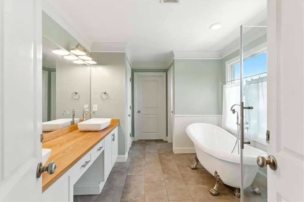 Bathroom with double vanity, crown molding, a freestanding tub, a wainscoted wall, and tile patterned flooring