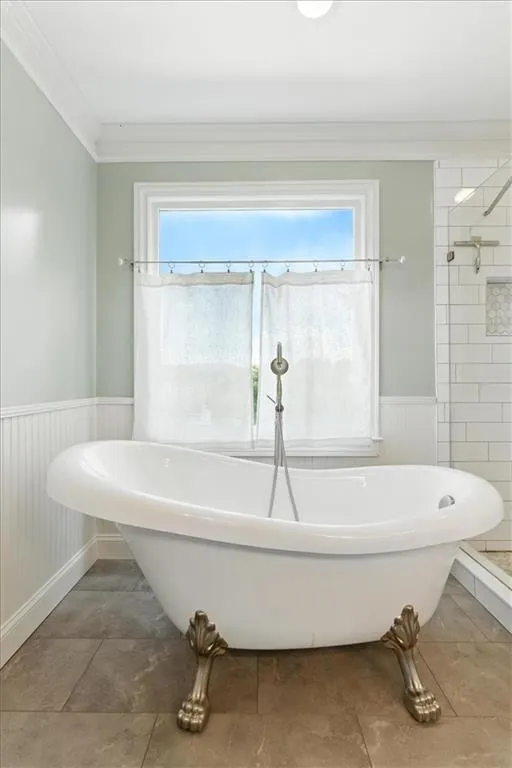Full bathroom with a wainscoted wall, crown molding, plenty of natural light, a soaking tub, and tiled shower