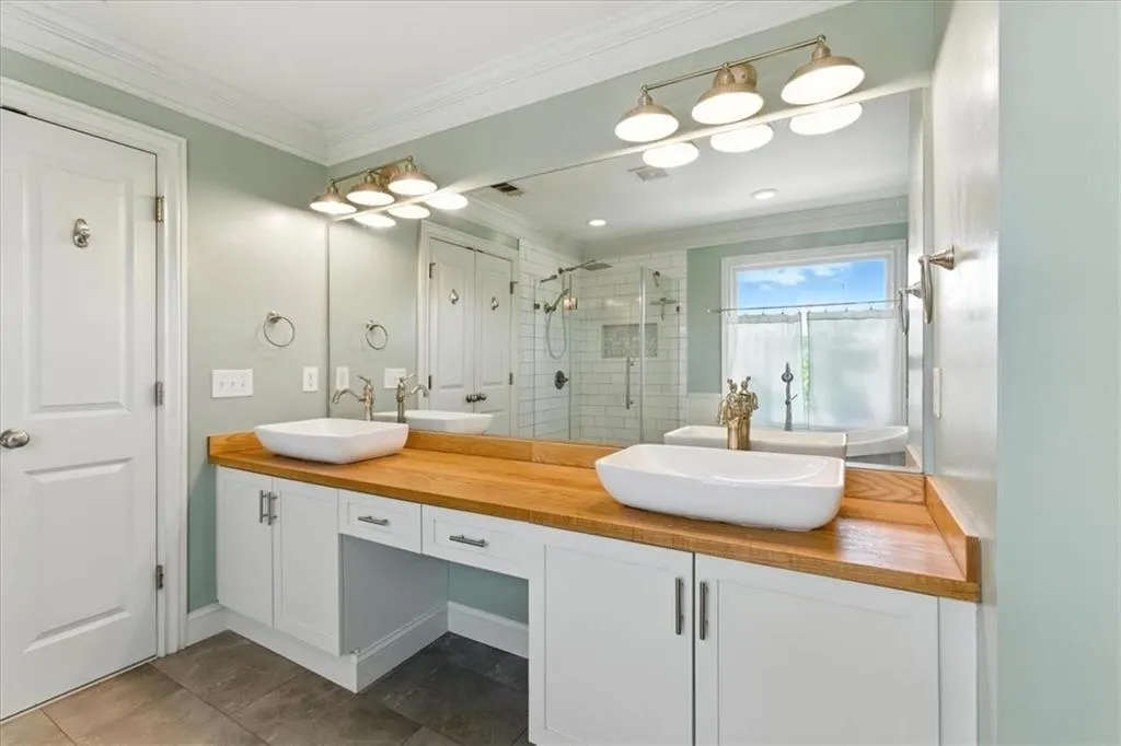 Bathroom with double vanity, a shower stall, ornamental molding, and tile patterned floors