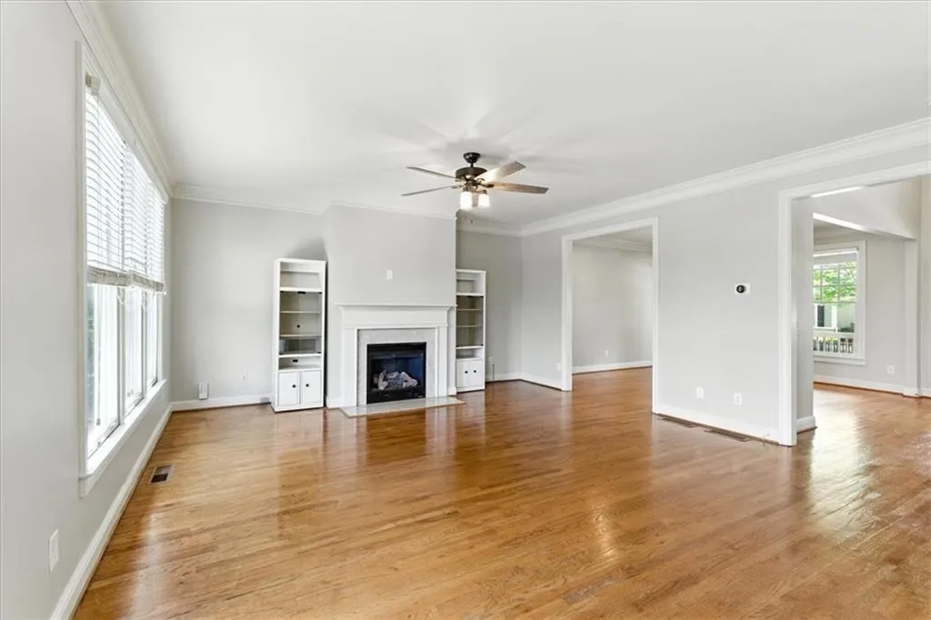 Unfurnished living room featuring light wood-type flooring, ceiling fan, crown molding, and a fireplace