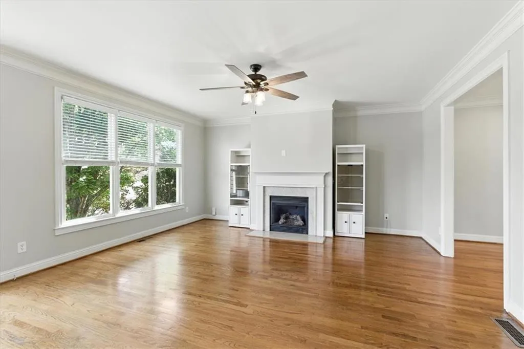 Unfurnished living room featuring ornamental molding, wood finished floors, a premium fireplace, and a ceiling fan
