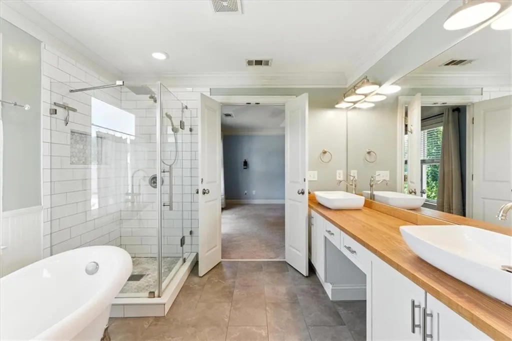 Full bath featuring double vanity, a freestanding tub, ornamental molding, a shower stall, and tile patterned floors
