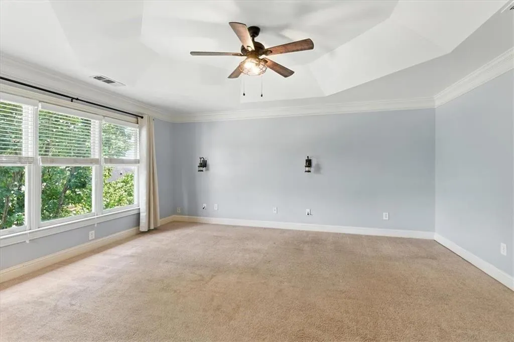 Empty room featuring light carpet, ornamental molding, a tray ceiling, and ceiling fan