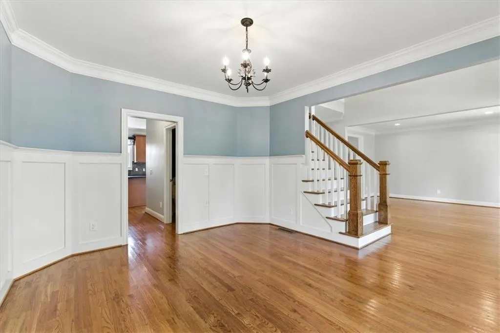 Unfurnished dining area featuring a decorative wall, wood finished floors, a chandelier, wainscoting, and stairway